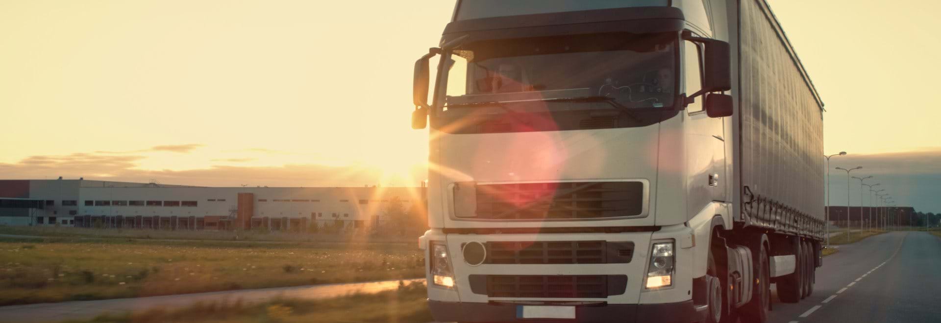 White truck leaving a warehouse against a sunset